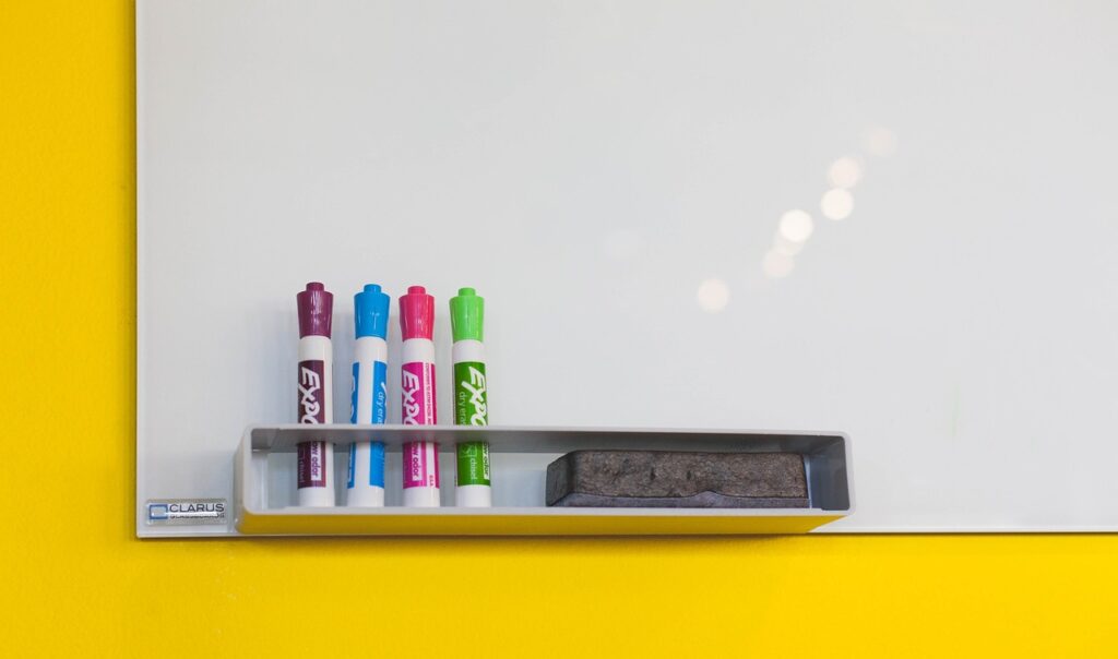 A corner of a whiteboard with a shelf holding Expo markers and an eraser.